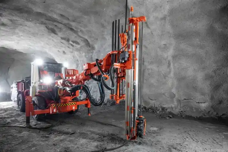 Sandvik Ranger DX surface top hammer drill rig shown in a mining or construction environment from a front-side angle. The yellow, self-propelled machine features a reinforced operator cabin, articulated drilling boom, and large rugged tires designed for precise and efficient surface drilling in quarrying and mining applications.